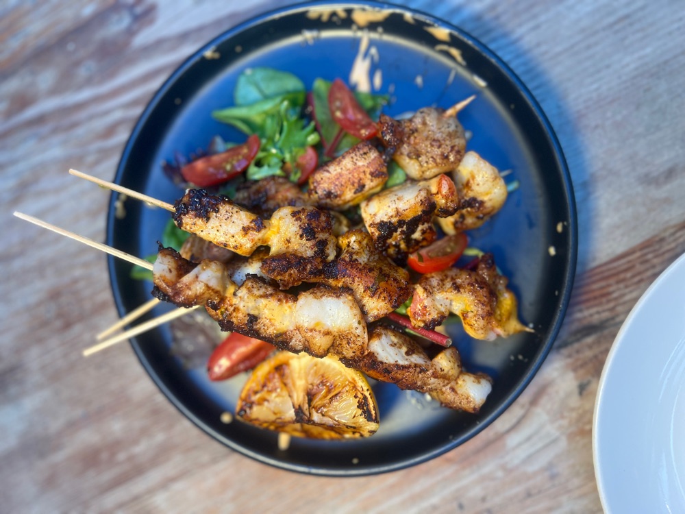 Grilled chicken and seafood skewers served on a blue plate